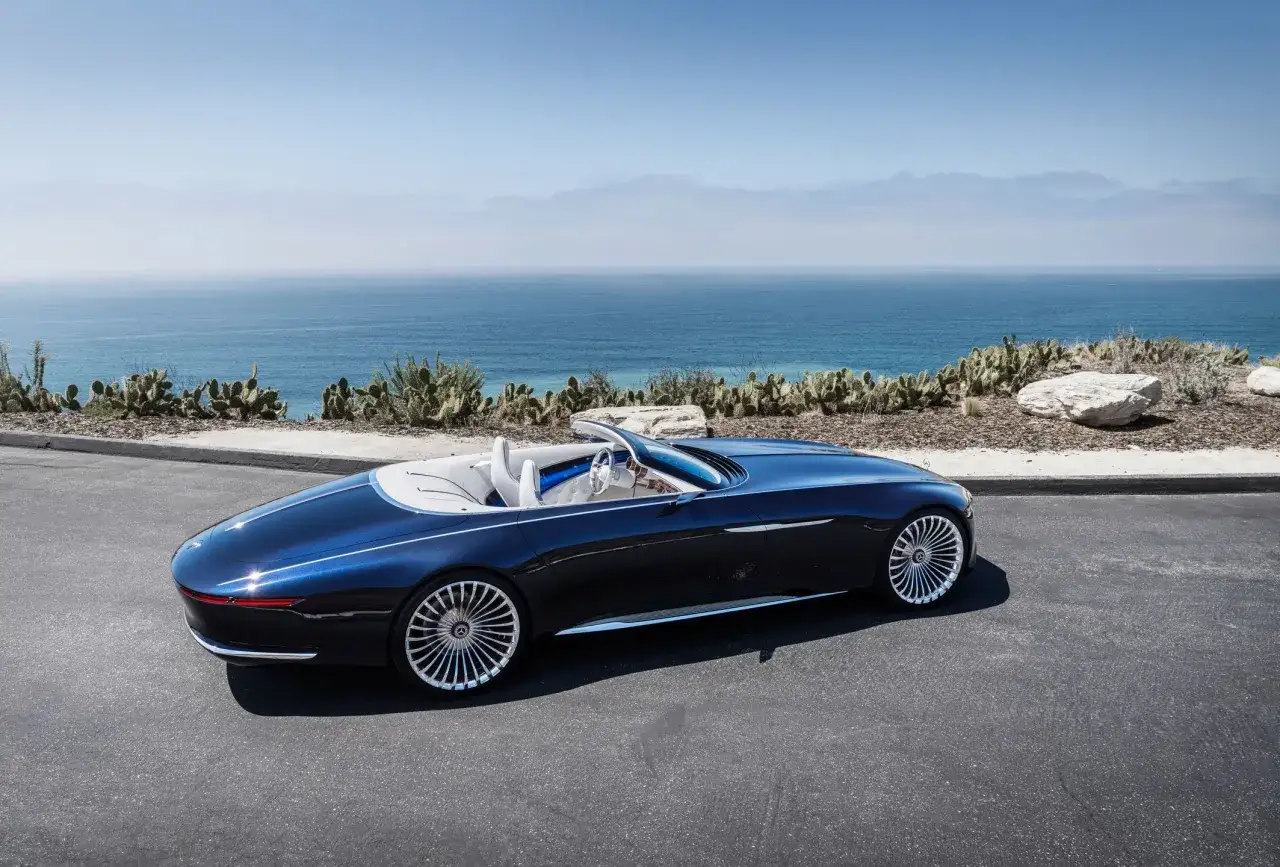 Elegancki, granatowy roadster z białym wnętrzem na tle błękitnego oceanu i kaktusów.