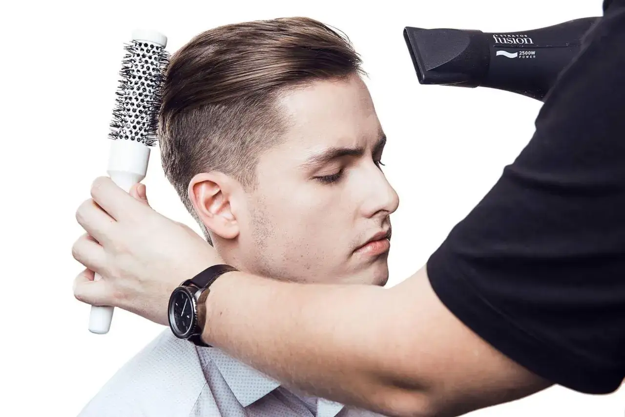 Stylista suszy i układa męskie włosy okrągłą szczotką. To klucz do tego, jak dbać o włosy męskie, by wyglądały perfekcyjnie.