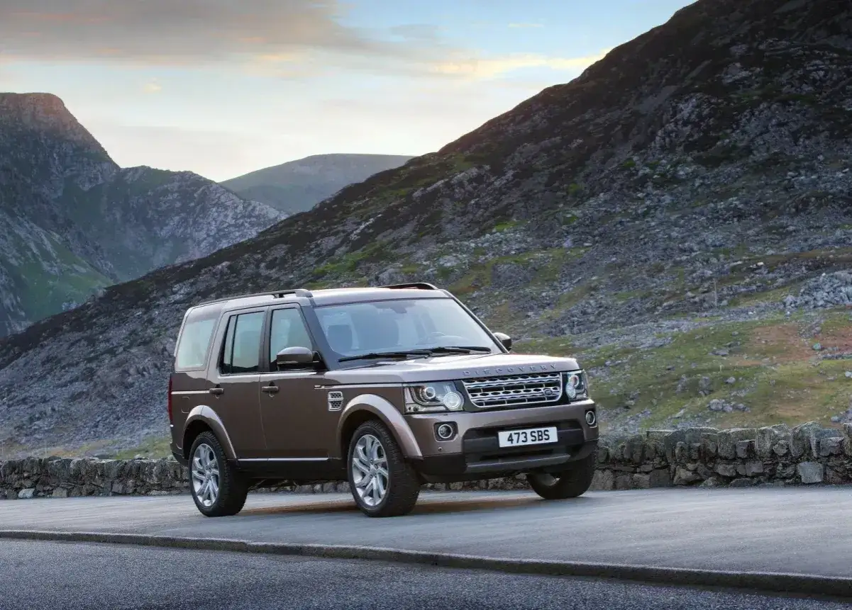 Brązowy Land Rover Discovery 4 na tle górskiej drogi. Nawet ten terenowy gigant może mieć **awarie i problemy**, ale jego wygląd wciąż budzi respekt.