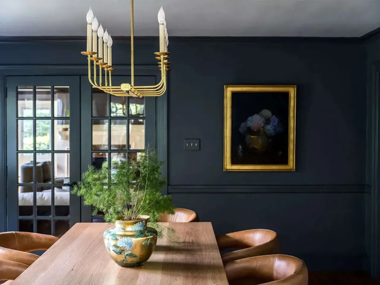 Ein goldener Kronleuchter und eine Vase mit Blumen auf einem Holztisch. Dunkelblaue W&auml;nde. Welche Farbe passt zu Gold? Hier: Braun, Blau und Gr&uuml;n.