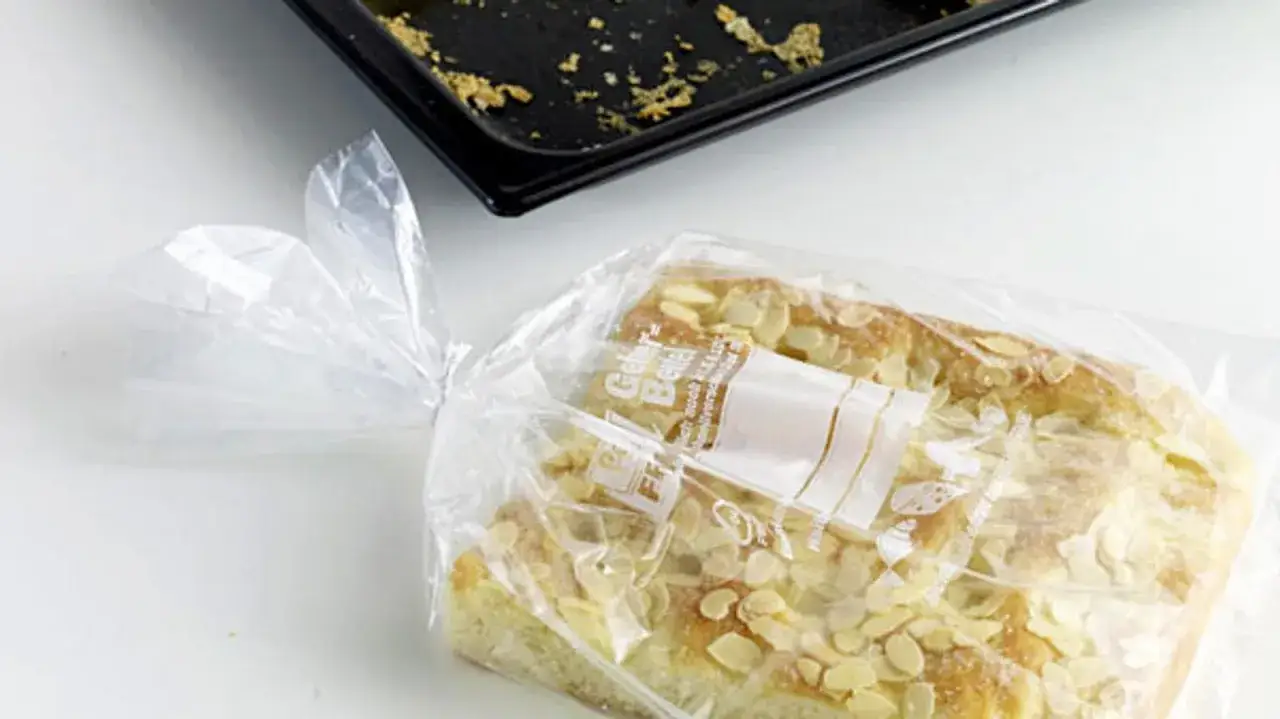 Ein mit Mandeln bestreuter Kuchen wird f&uuml;r das Kuchen einfrieren in eine Plastikt&uuml;te verpackt. Daneben liegt eine leere Backform.