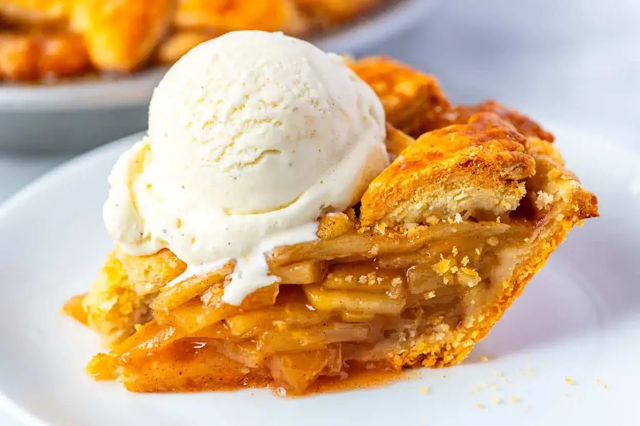 Una porción de tarta de manzana tradicional, dorada y crujiente, coronada con una bola de helado de vainilla que se derrite.