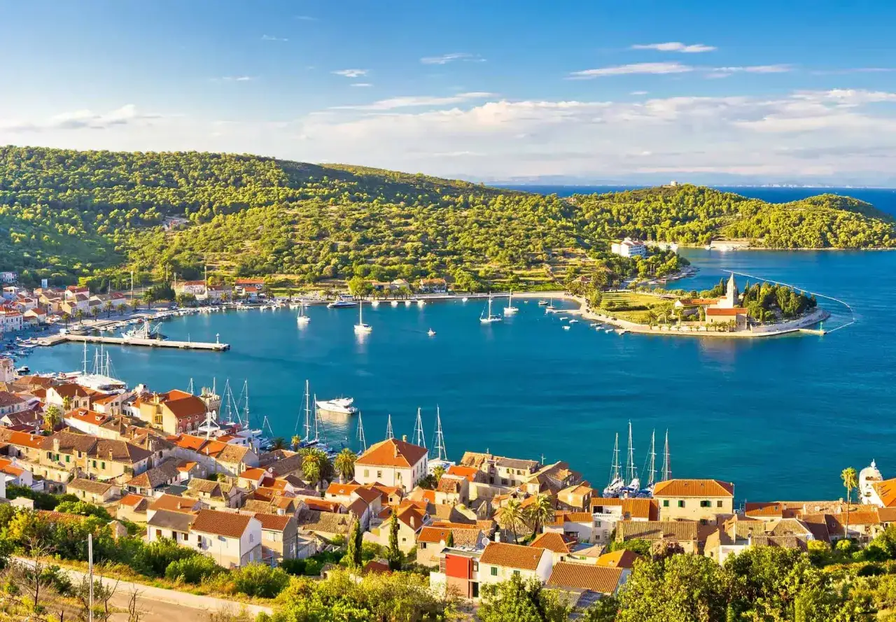 Vacker vy &ouml;ver Vis, Kroatien. En charmig stad med r&ouml;da tak och en turkos bukt fylld med segelb&aring;tar.
