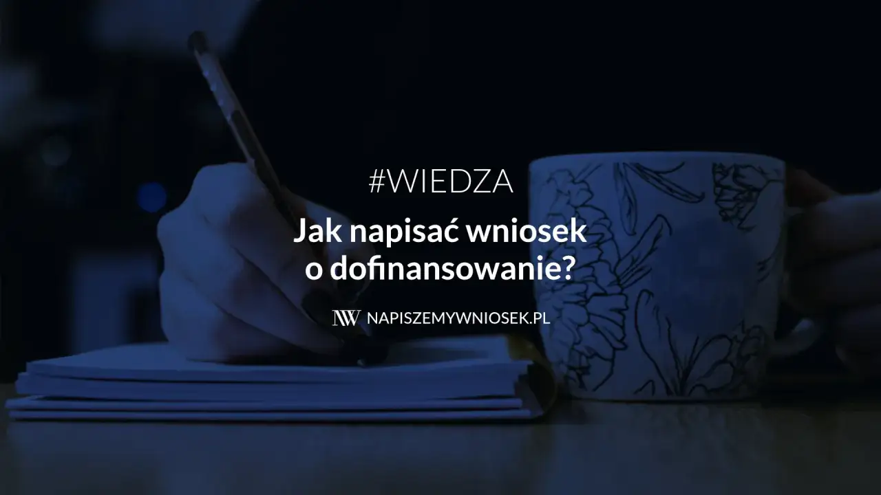 Dłoń pisze piórem na notatniku, obok kubek z napisem