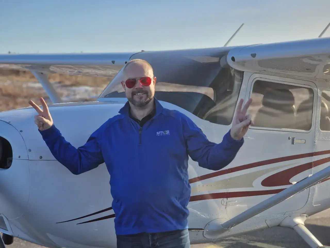 Fredrik Bruhn, glad i solglas&ouml;gon, g&ouml;r fredstecken framf&ouml;r ett litet flygplan.