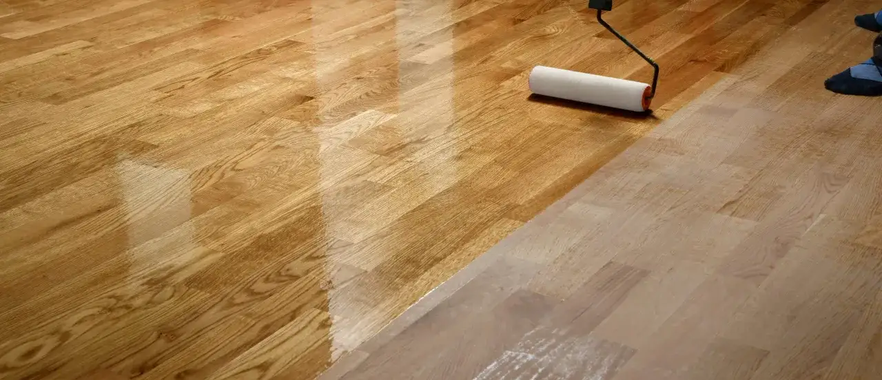 Un rullo stende le vernici su un parquet in legno, creando una finitura lucida e protettiva.