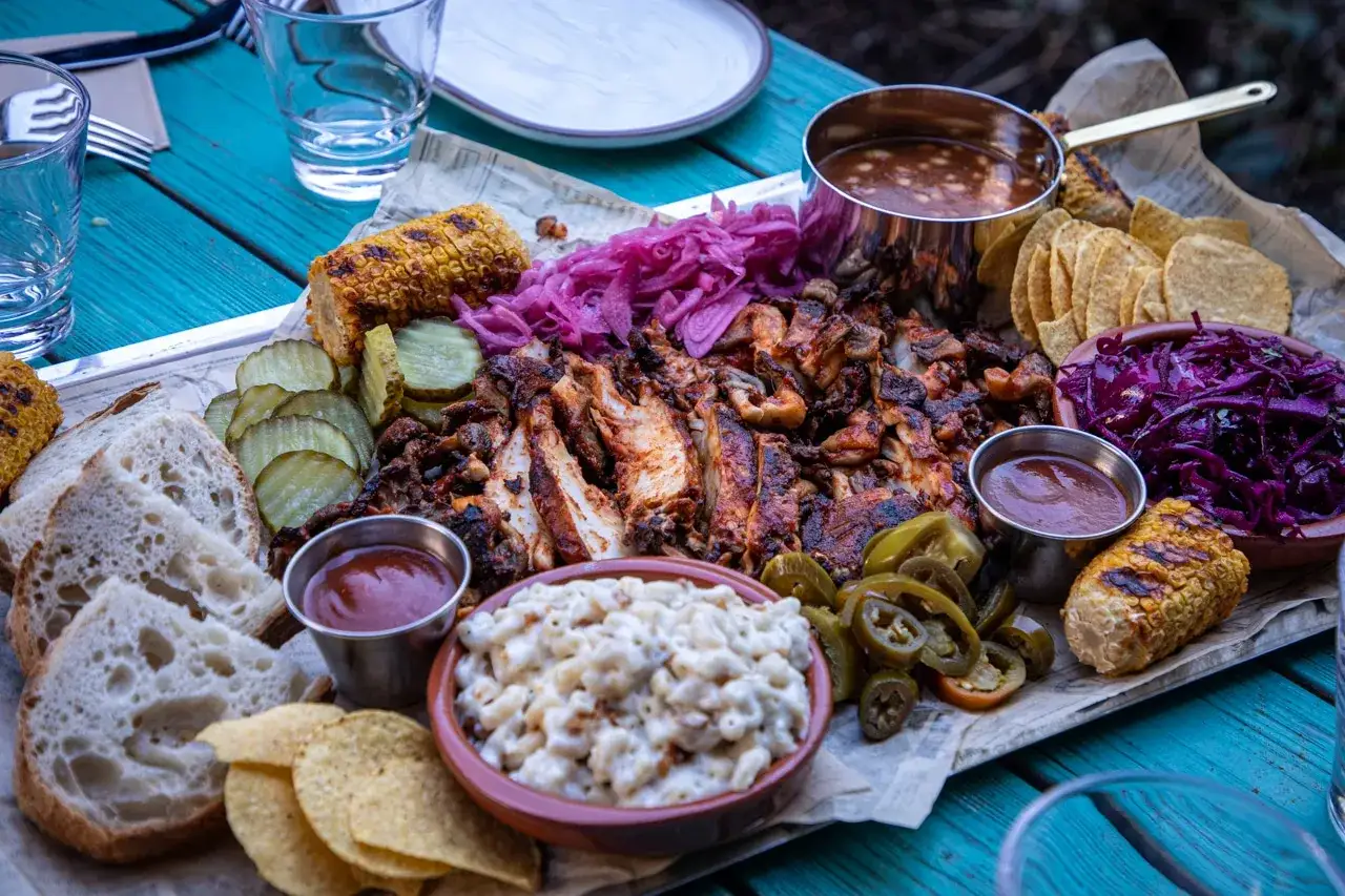 En härlig bricka med tillbehör för att grilla veganskt: majskolvar, picklad rödlök, picklad gurka, bröd, mac and cheese, jalapeños och bönor.