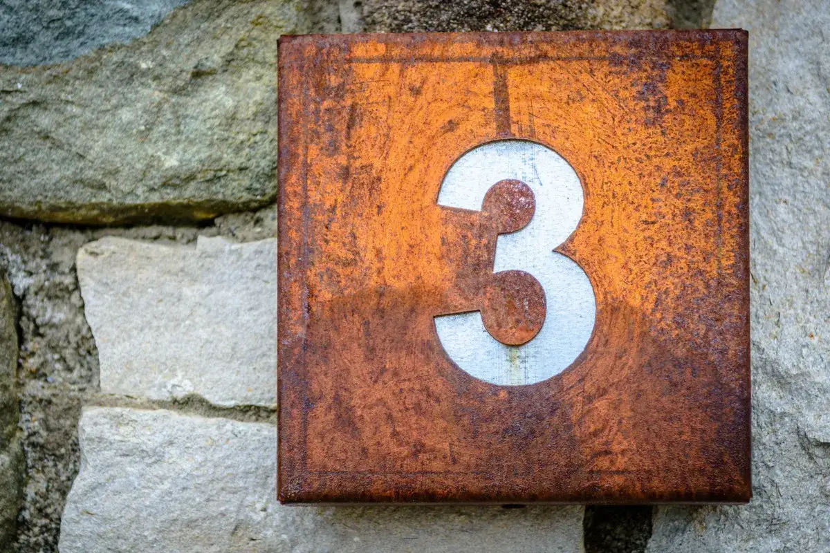 Zardzewiała tabliczka z numerem 3, niczym symbol numerologiczna 3, przyczepiona do kamiennej ściany.