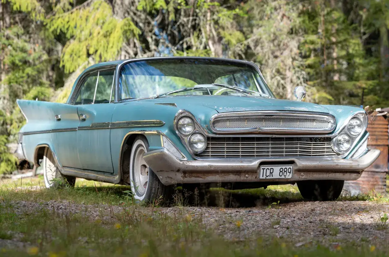 En turkos de soto bil med fenor st&aring;r parkerad i skogen.