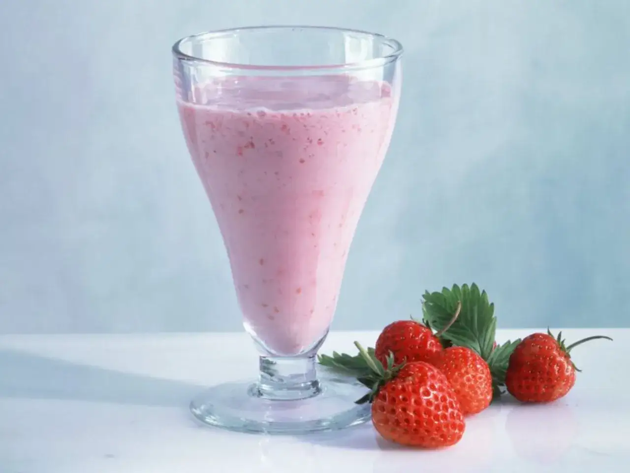 Ein cremiger Erdbeer Milchshake im Glas, daneben frische Erdbeeren mit Blättern.