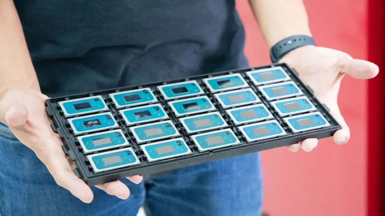 Dłonie trzymają tackę z rzędem nowych procesorów Intel.