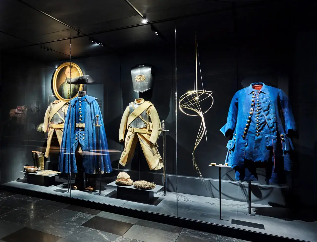 Kungliga Livrustkammaren visar historiska dräkter, rustningar och vapen. Här syns en blå uniform, en gul jacka med byxor, en bröstplåt och en porträttmålning.