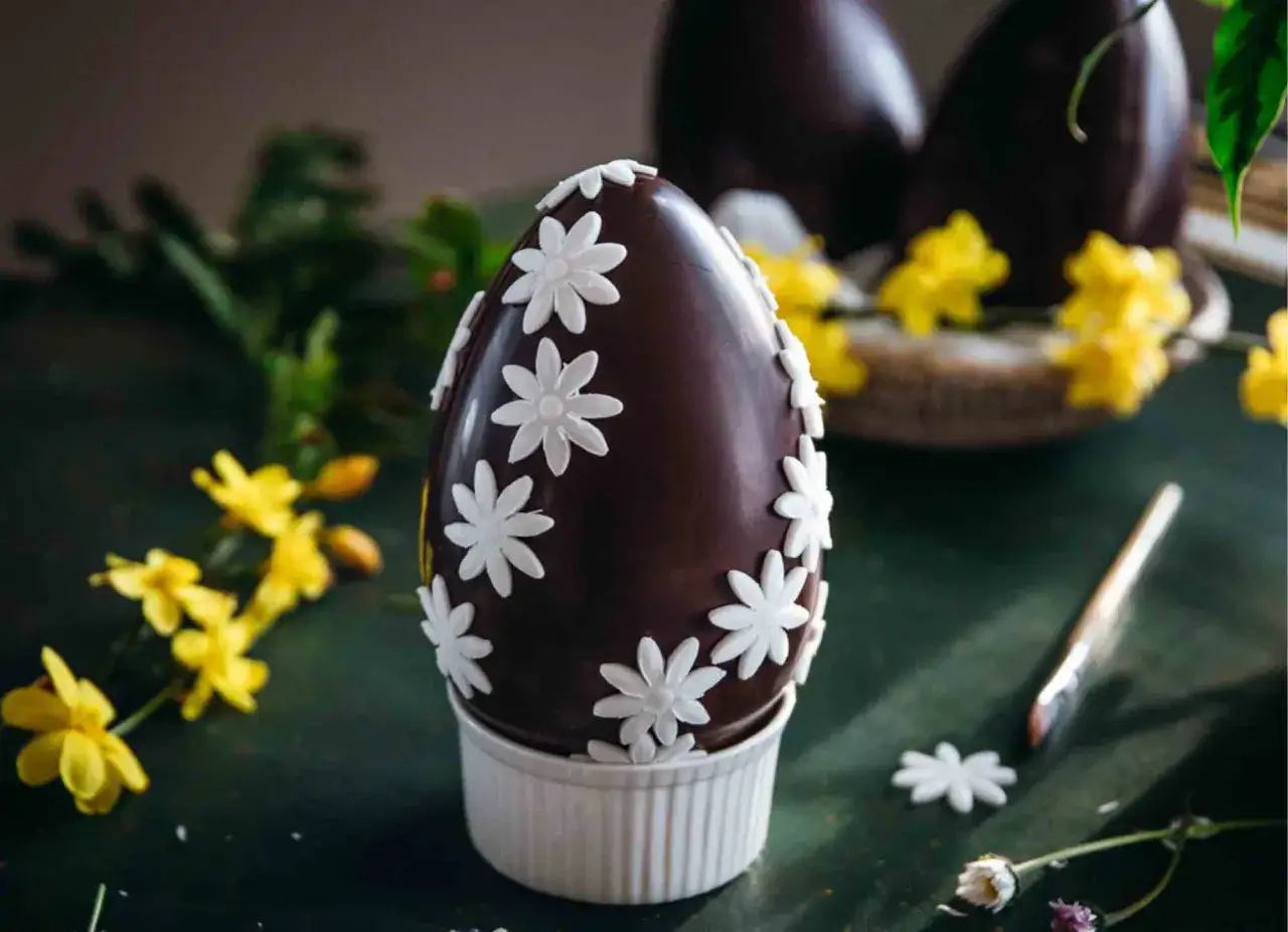 Uovo di Pasqua al cioccolato decorato con fiori bianchi, come disegni da colorare uova di pasqua. Gialli fiori primaverili sullo sfondo.