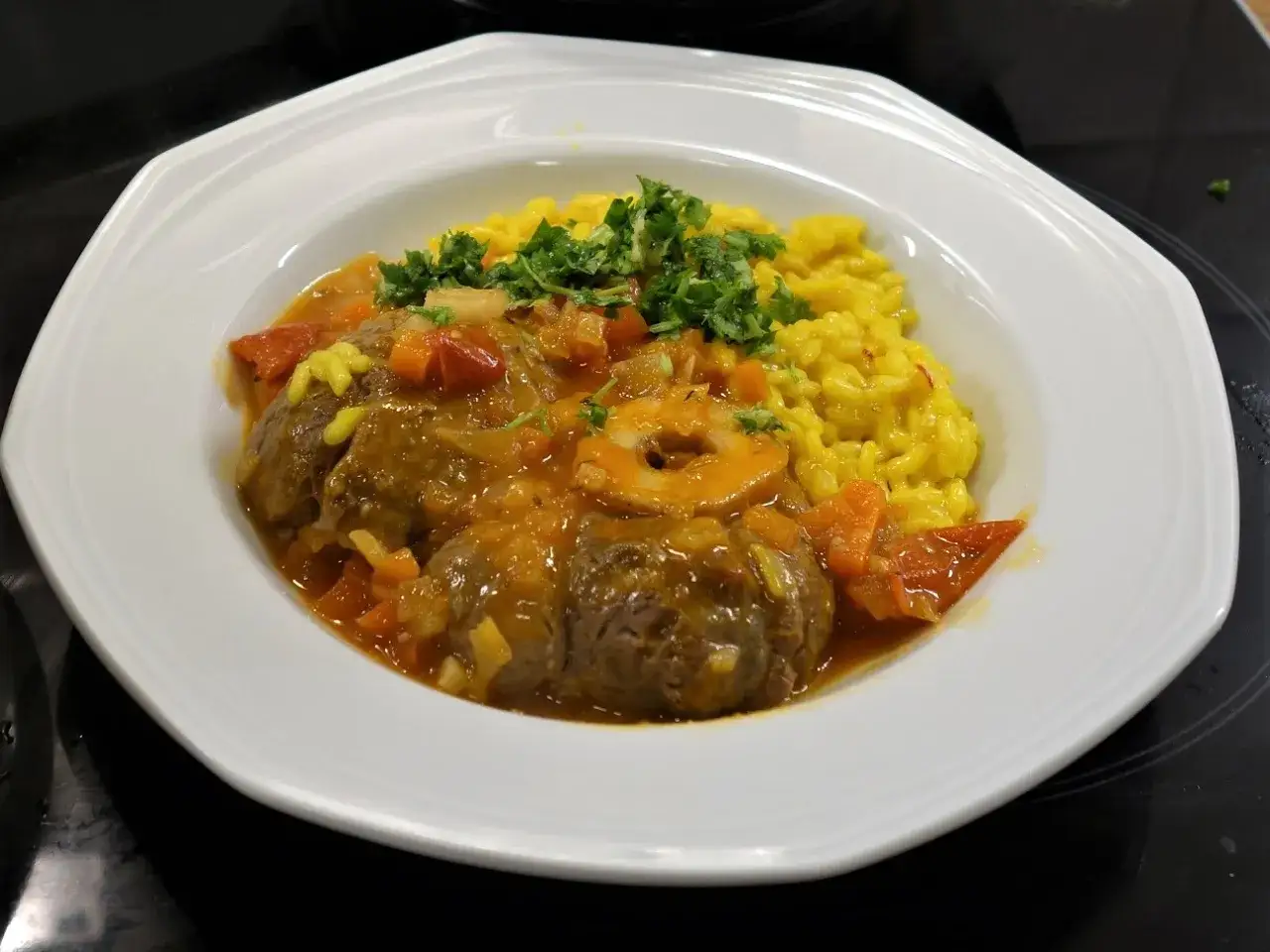 En tallrik med osso buco, saftigt kalvl&auml;gg i en mustig s&aring;s med tomater och mor&ouml;tter, serverad med gyllene saffransrisotto och f&auml;rsk persilja.
