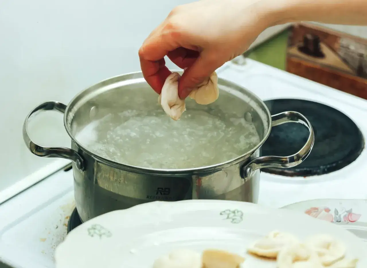 Ręka wrzuca pierogi do gotującej się wody. Tak blanszować pierogi, by były idealne.