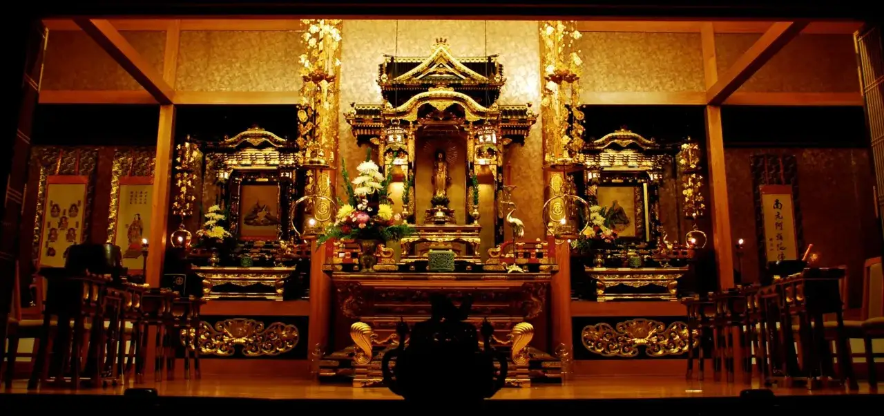 Ett gyllene buddhistiskt tempel med detaljerade altare, blommor och statyer. En fridfull plats f&ouml;r meditation.