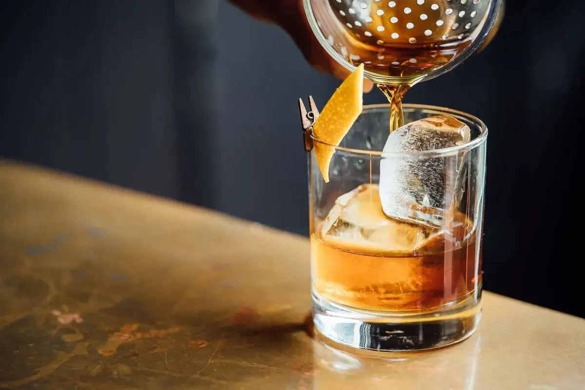 En drink h&auml;lls upp i ett glas med is och en apelsinzest, som en del av ett old fashioned recept.
