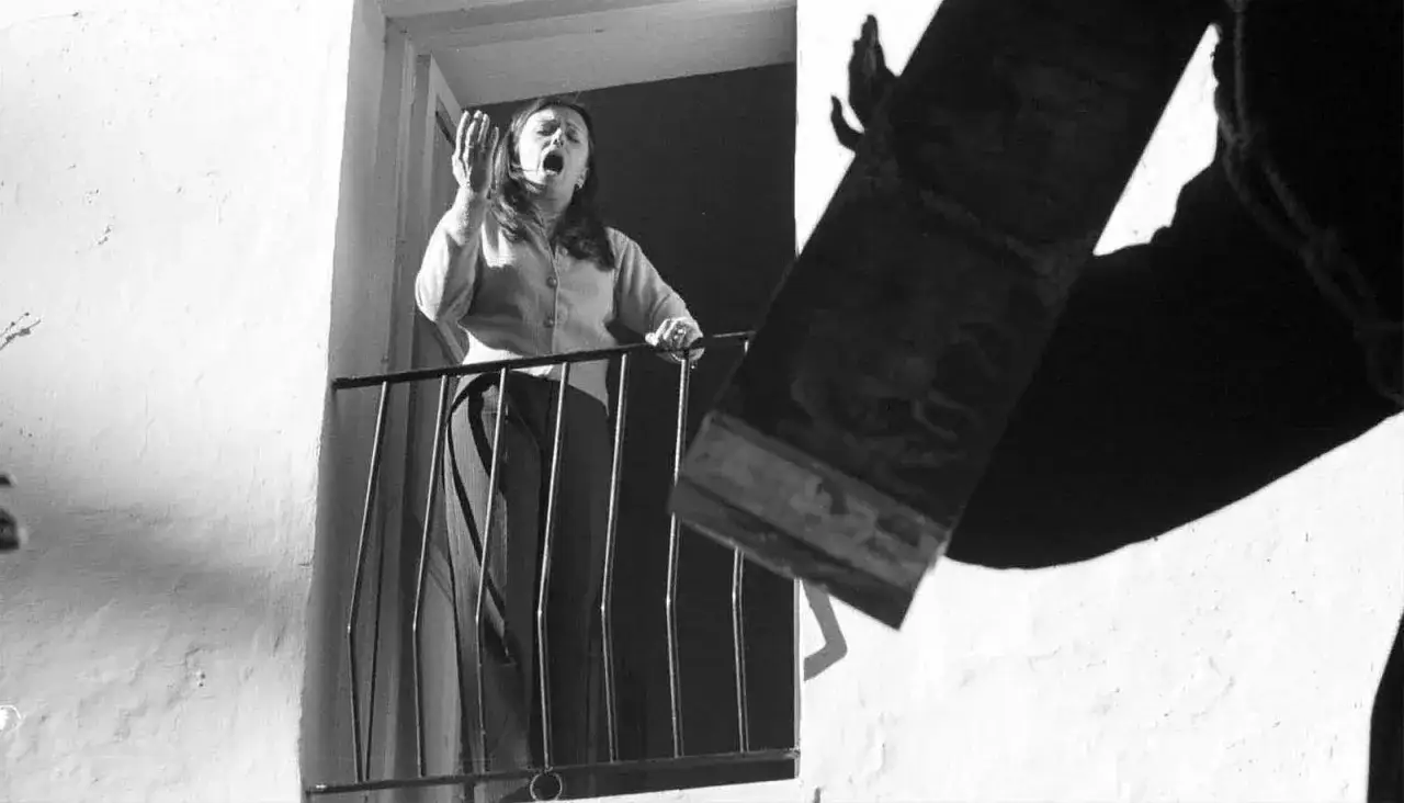Mujer en balcón, con la boca abierta, parece cantar o gritar, quizás una de las **saetas populares** que resuenan en la calle.