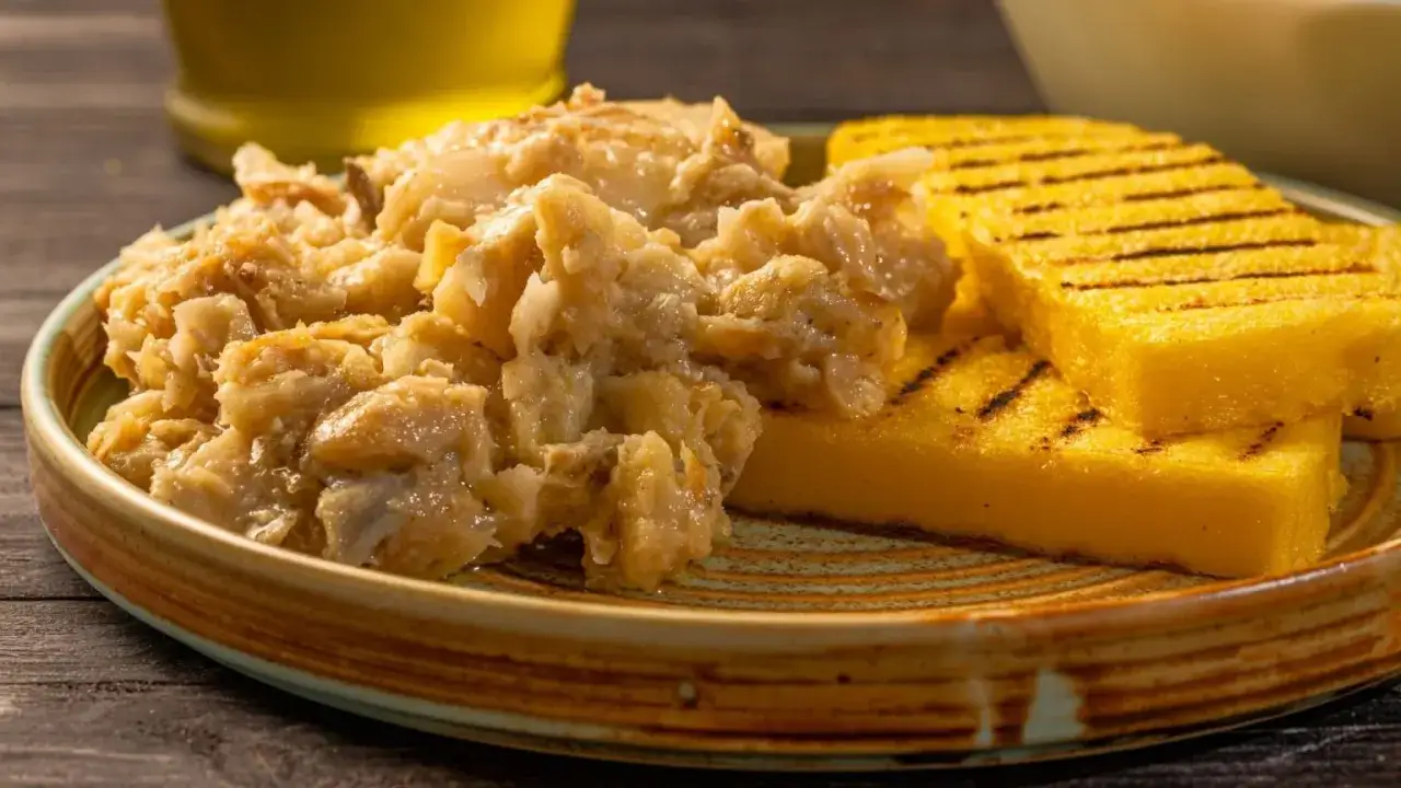 Baccal&agrave; alla Vicentina, ein cremiges Stockfischgericht, serviert mit gegrillter Polenta auf einem rustikalen Teller.
