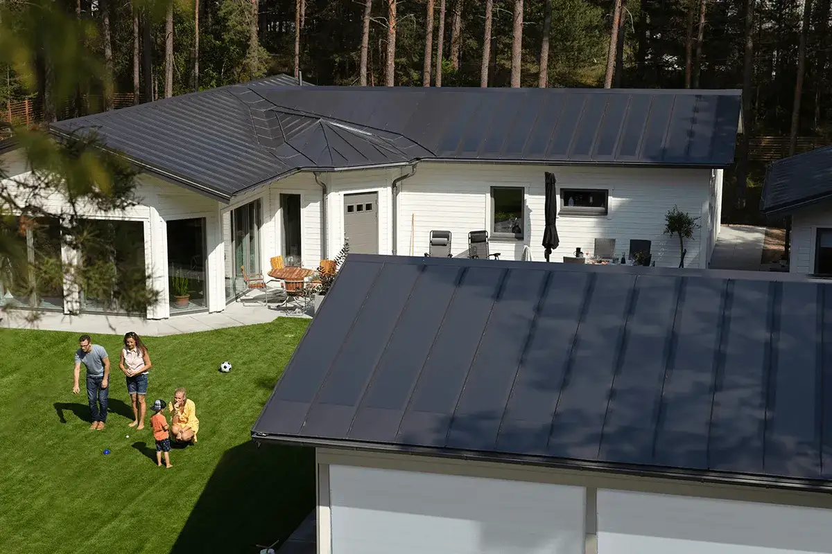 Familj njuter av solen p&aring; gr&auml;smattan framf&ouml;r ett modernt hus med ett stilrent lindab solar roof.