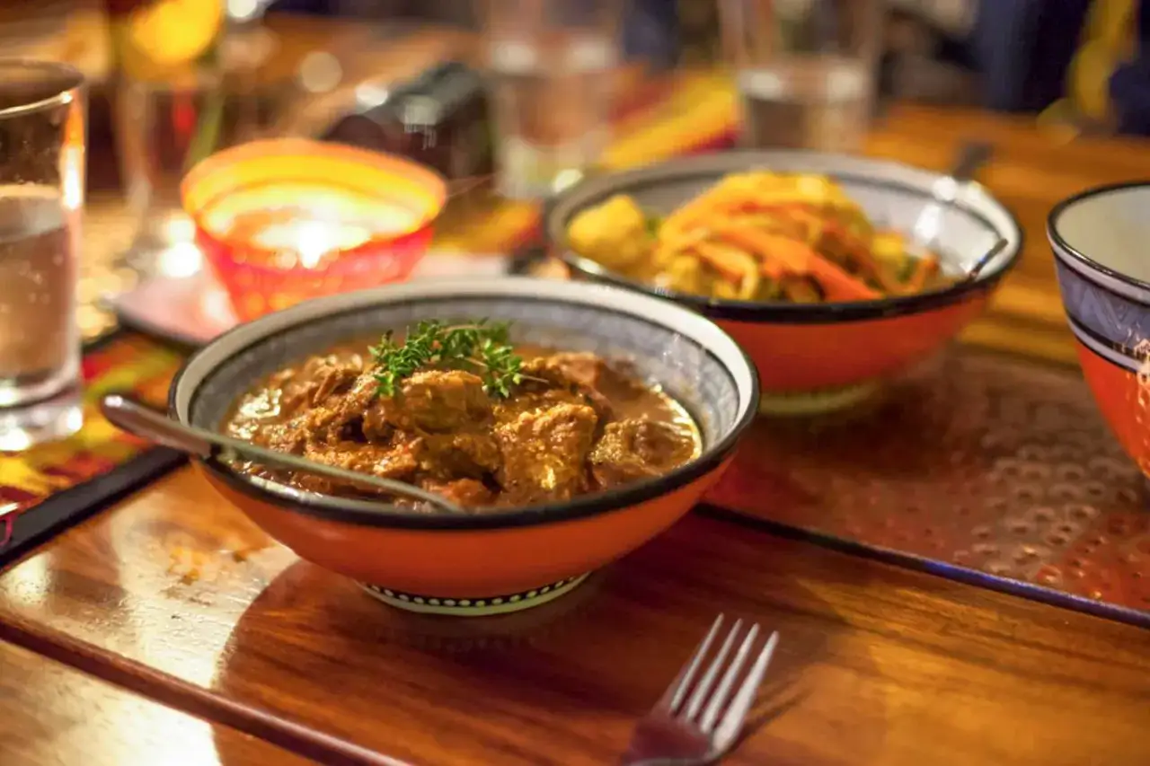 En sk&aring;l med mustig sydafrikansk mat, en gryta med k&ouml;tt och &ouml;rter, st&aring;r p&aring; ett tr&auml;bord. En annan sk&aring;l med gr&ouml;nsaker syns i bakgrunden.