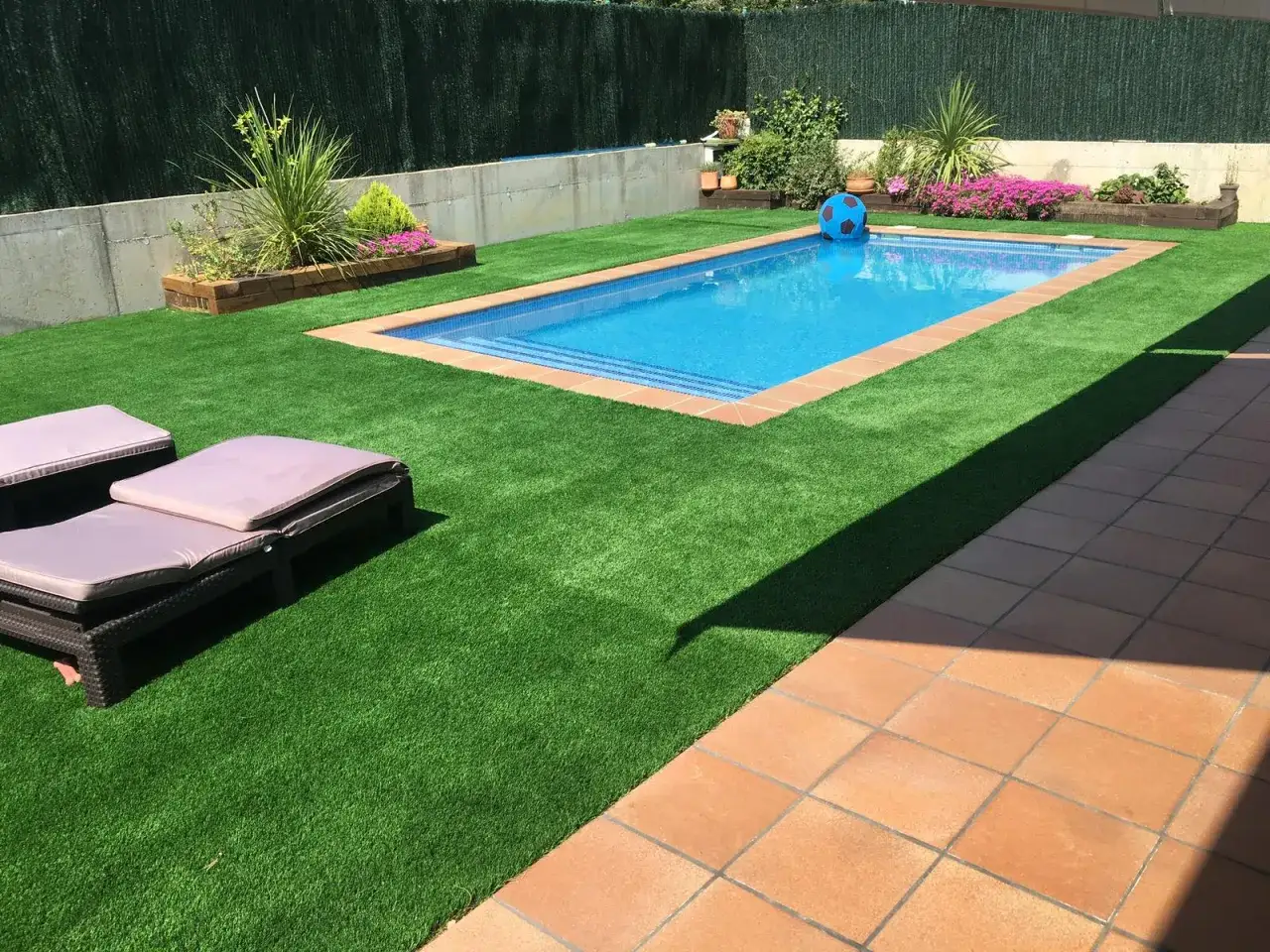 Un jardín con piscina y césped artificial verde vibrante. Las tumbonas invitan al descanso. Pregúntate: ¿cuánto dura el césped artificial?