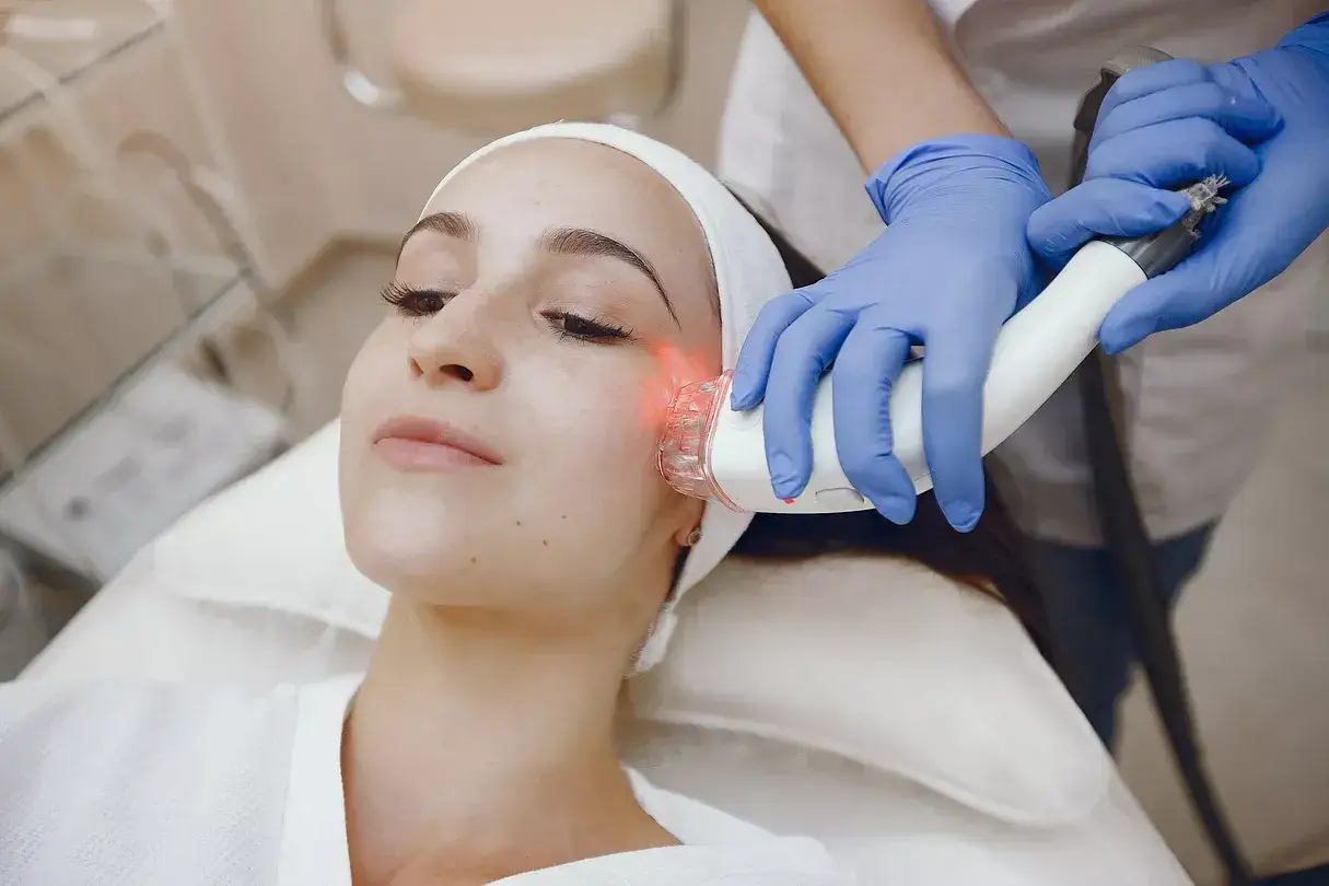 En kvinna f&aring;r en behandling med laser ansikte. En hudterapeut anv&auml;nder en apparat f&ouml;r att behandla hennes hud.