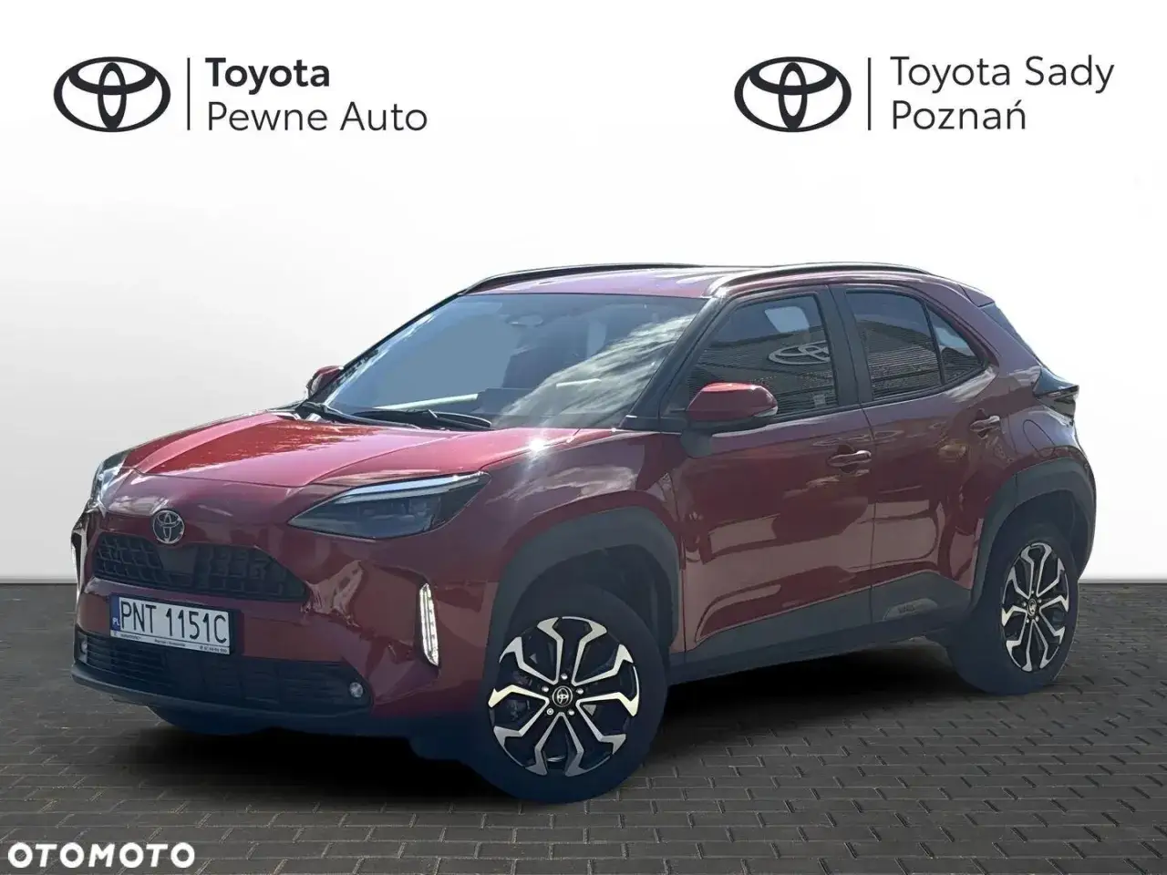 Czerwony Toyota Yaris Cross, który może mieć pewne wady, stoi na tle białej ściany i logo 