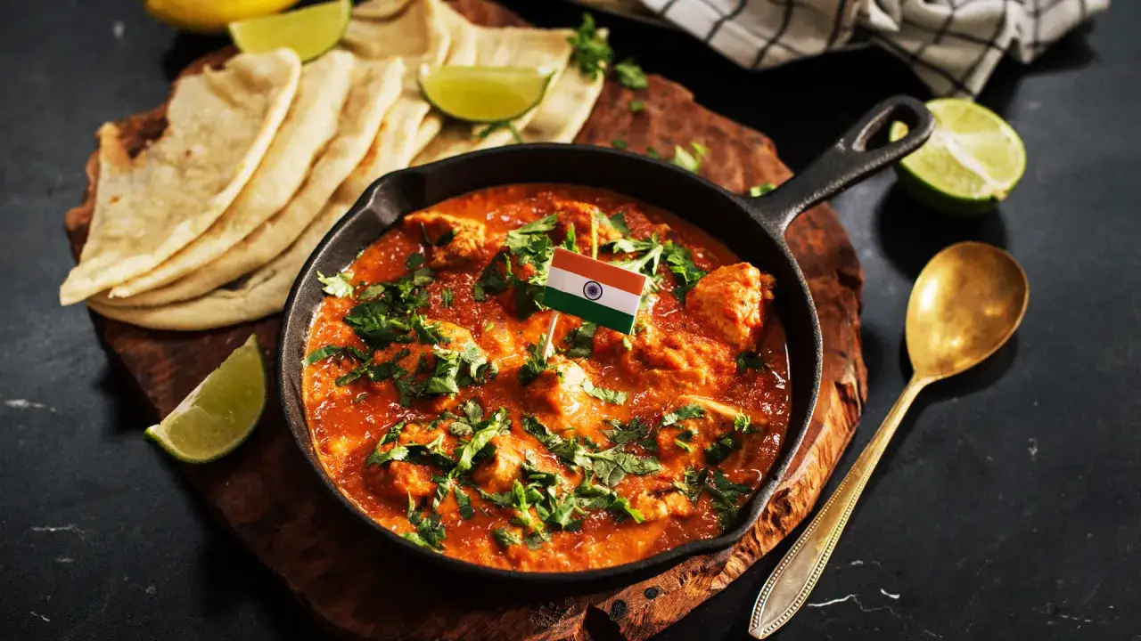 Aksamitny butter chicken z chlebkiem naan, ozdobiony flagą Indii, podany z limonką i złotą łyżką.