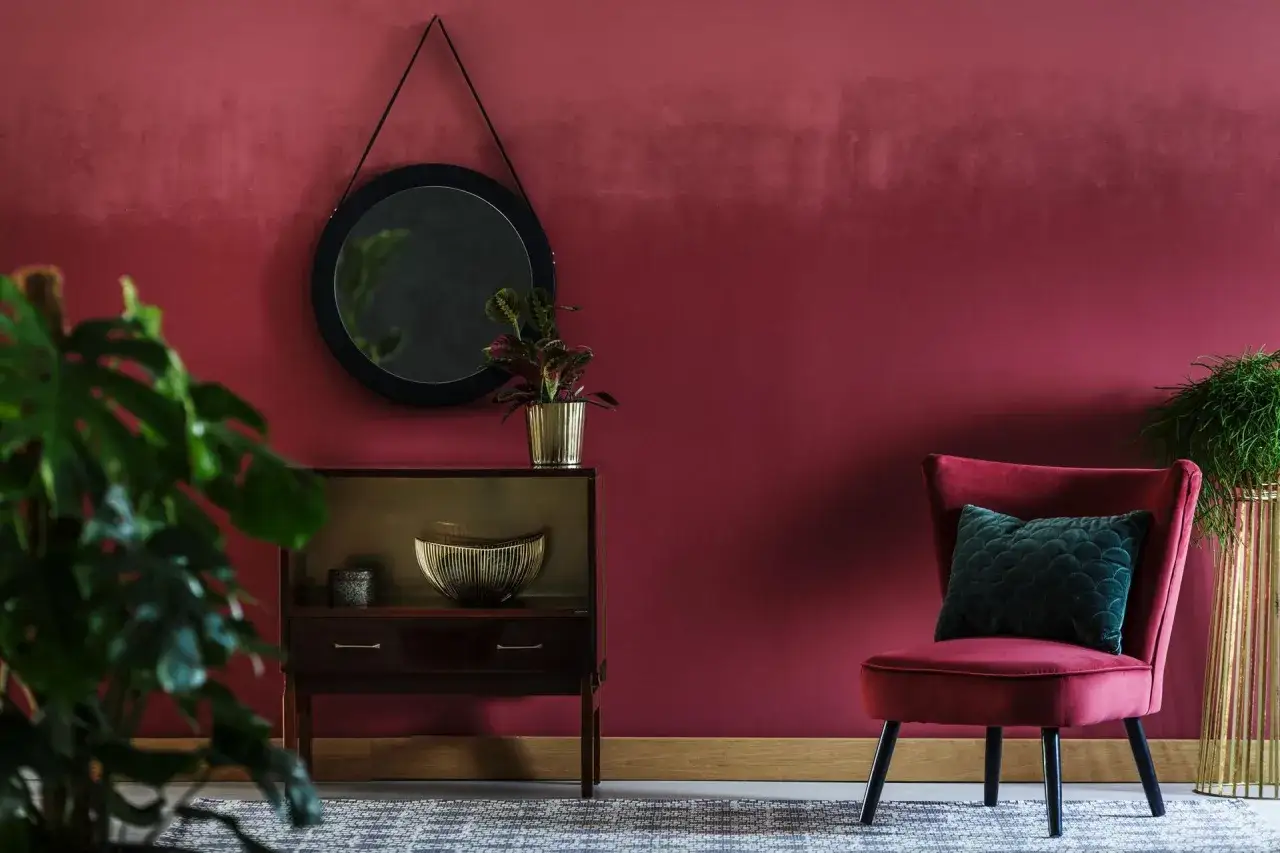 Eleganckie wnętrze z **burgundową** ścianą, aksamitnym fotelem i stylową komodą.
