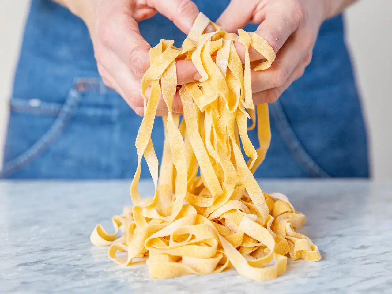 Mains d'un chef italien tenant des tagliatelles fraîches, prêtes pour une recette de pâtes maison.