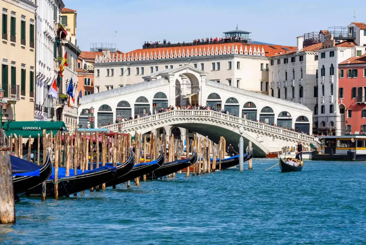 Gondoles bleues et noires amarr&eacute;es, le c&eacute;l&egrave;bre pont du Rialto &agrave; Venise se dresse majestueusement sur le Grand Canal, anim&eacute; par des touristes.