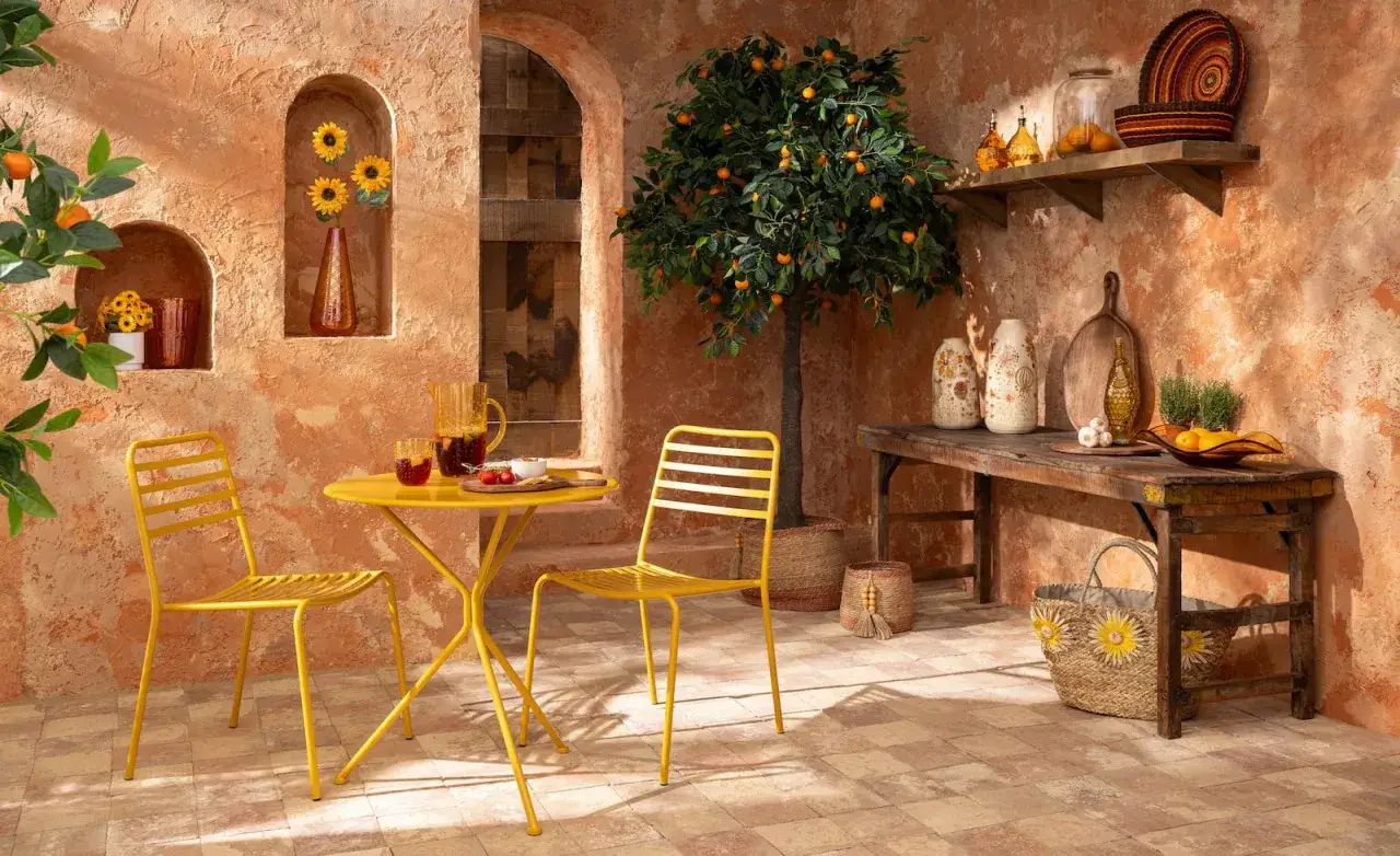 Terrasse ensoleill&eacute;e aux couleurs terracotta et jaune. Table et chaises jaunes, oranger, vases et paniers d&eacute;corent cet espace m&eacute;diterran&eacute;en.