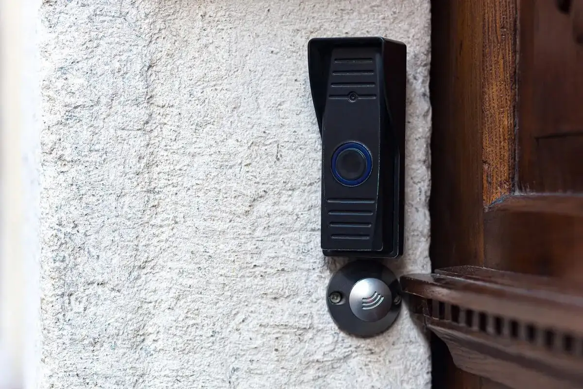 Sonnette moderne sur mur texturé, près d'une porte en bois. Idéal pour la réparation sonnette locataire ou propriétaire.
