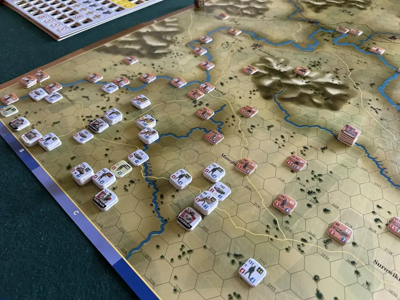 Plansza gry strategicznej z żetonami wojsk, rzeką i wzgórzami. Widać fragmenty mapy, które przywołują klimat **old world**.