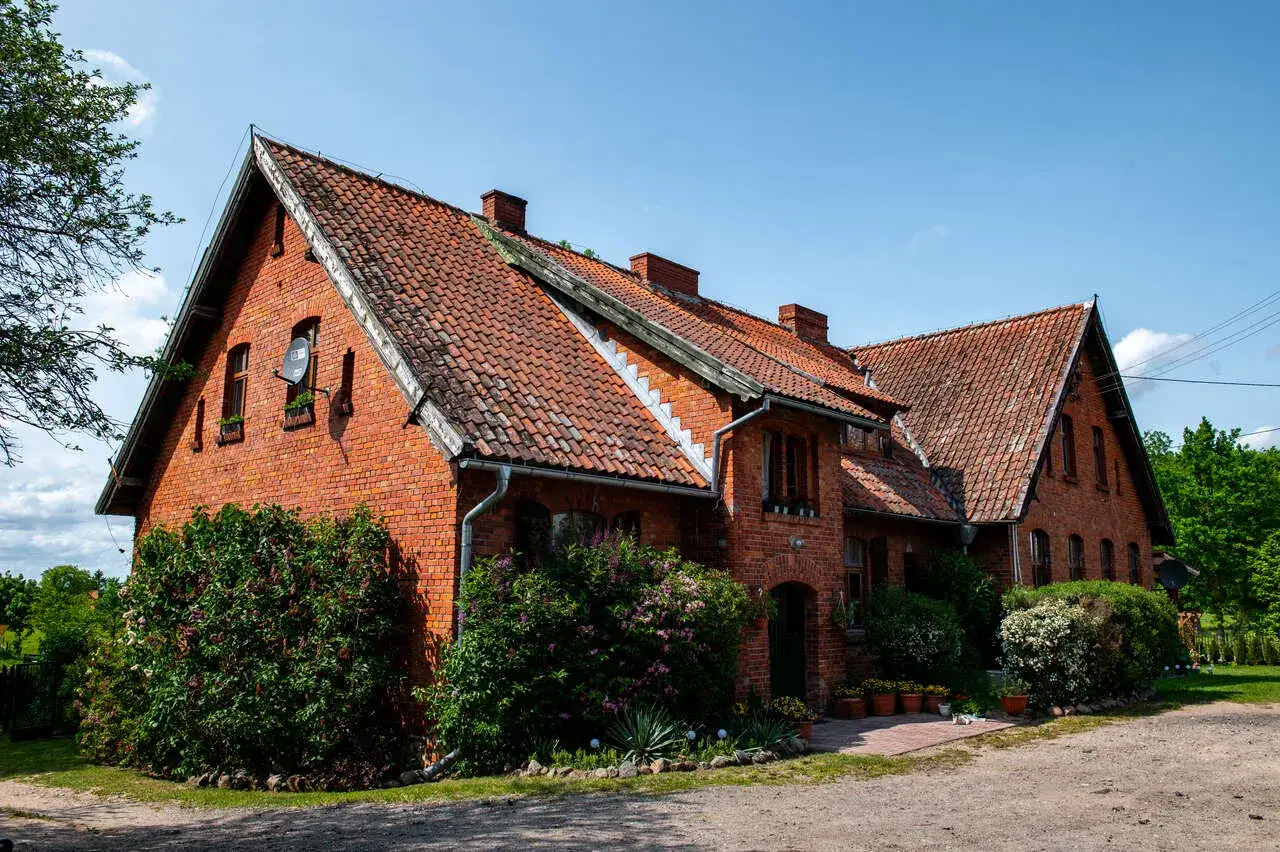 Stary ceglany dom z czerwonym dachem, otoczony zielenią. Zastanawiasz się, ile lat musi mieć dom, żeby był zabytkiem?