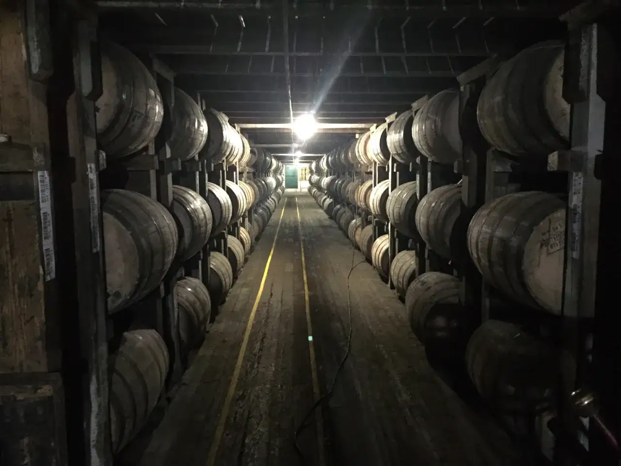 Rzędy beczek z whisky w ciemnej piwnicy, gdzie część trunku znika jako whisky angel share.