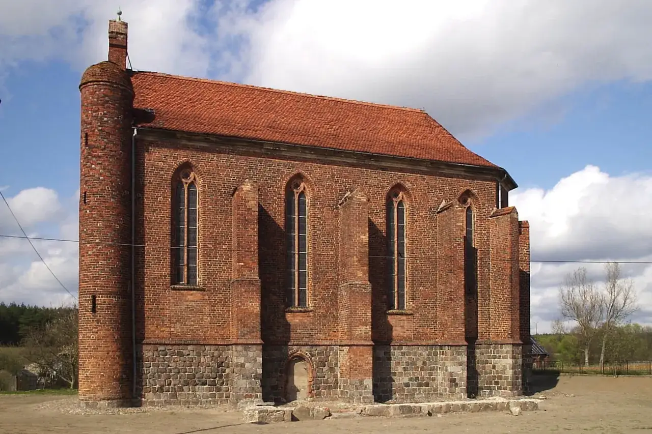 Gotycka budowla z cegły, przypominająca dawną warownię templariuszy, z charakterystyczną wieżyczką i strzelistymi oknami.