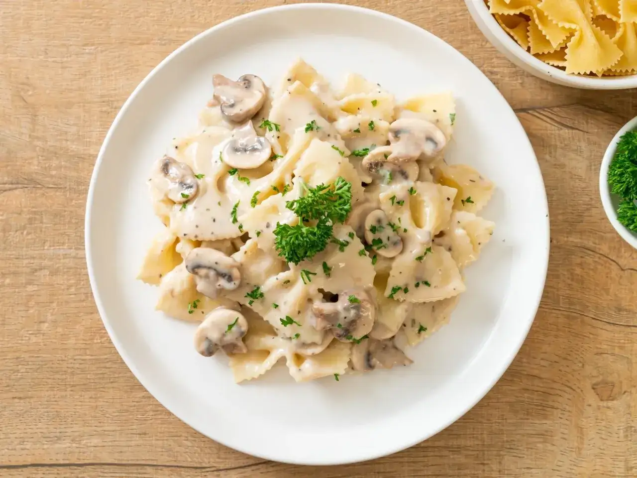 Pyszne farfalle w kremowym sosie grzybowym, idealne na trzy pomysły na szybki obiad z makaronem. Posypane natką pietruszki.