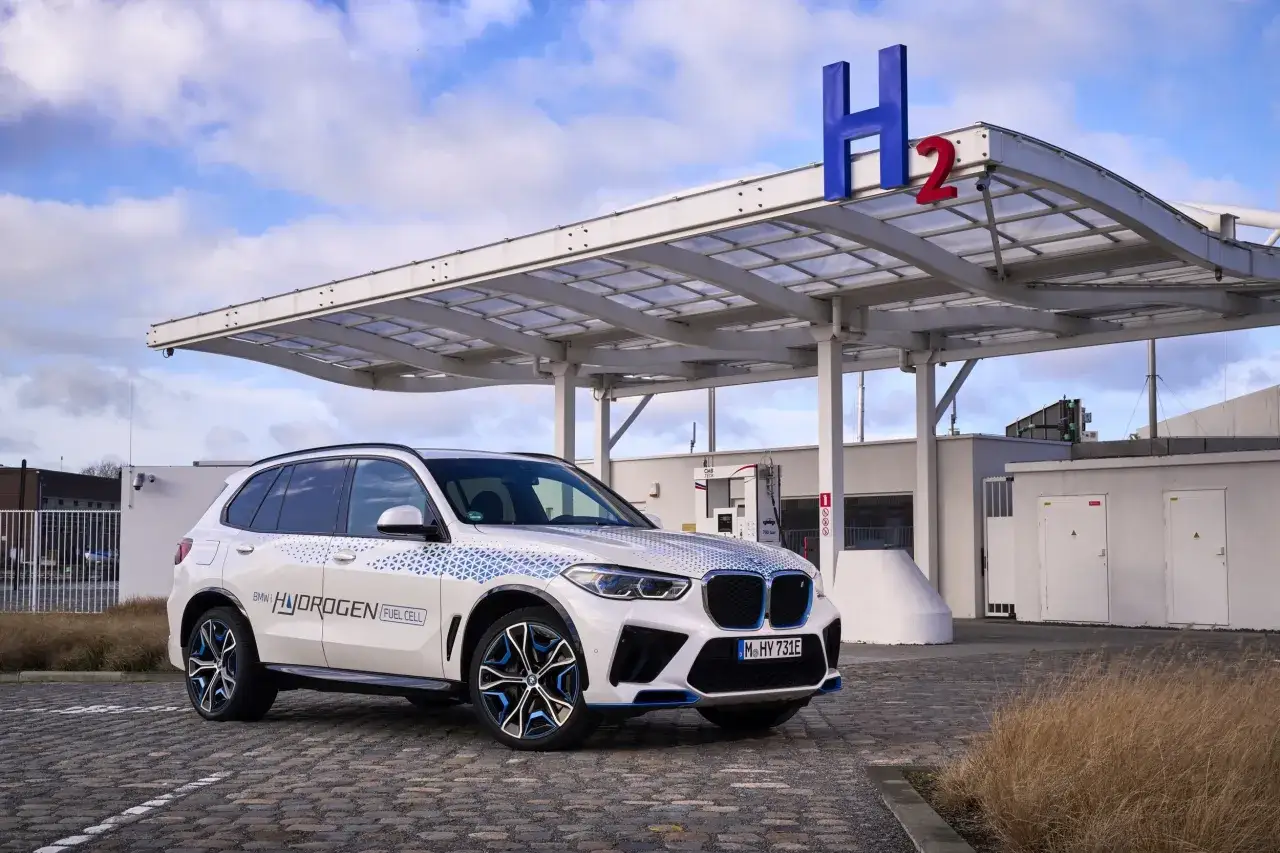 Biały BMW iX5 Hydrogen Fuel Cell na tle stacji tankowania wodoru.