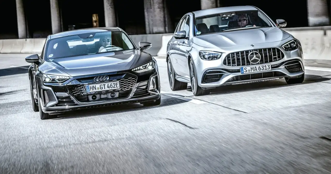 Dwa sportowe samochody, lśniące Audi i srebrny Mercedes, pędzą po drodze.