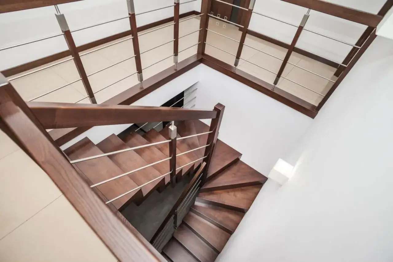 Eleganckie, drewniane schody do domu z metalową balustradą prowadzą na piętro.