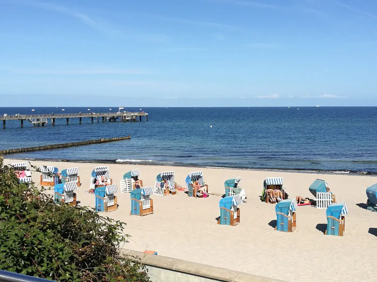 Wittenbeck Strand: Strandkörbe stehen bereit für sonnige Tage am Meer. Ein langer Pier ragt ins blaue Wasser.