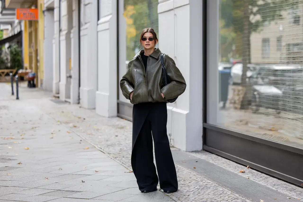 Kobieta w oliwkowej kurtce i czarnych spodniach wide leg, które dodają jej sylwetce lekkości i elegancji.