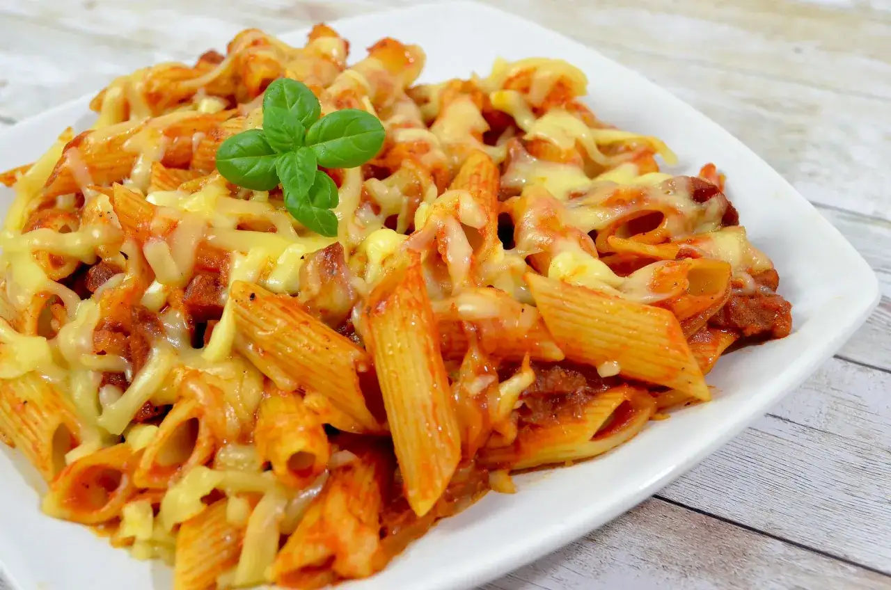 Penne z sosem pomidorowym i kawałkami pikantnego chorizo, zapieczone pod ciągnącym się serem, ozdobione listkiem bazylii.