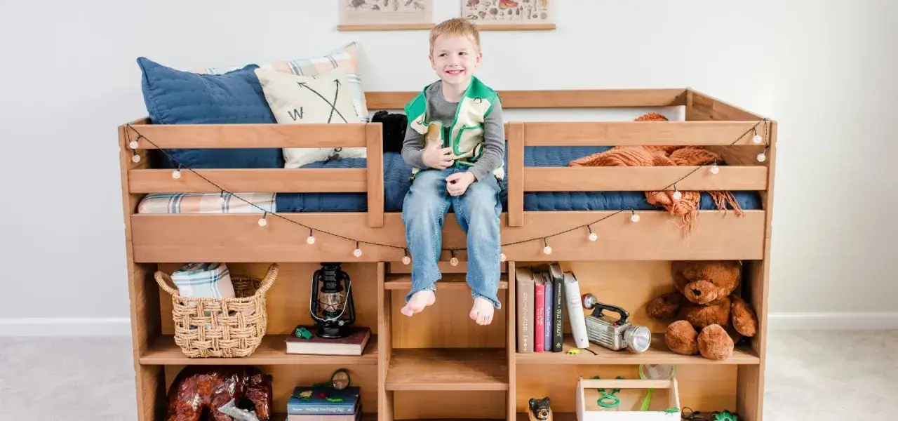 Ein Junge sitzt auf einem Hochbett, das mit B&uuml;chern, Spielzeug und Lichterketten eingerichtet ist. Perfekt, um ein Kinderzimmer mit Hochbett einzurichten.