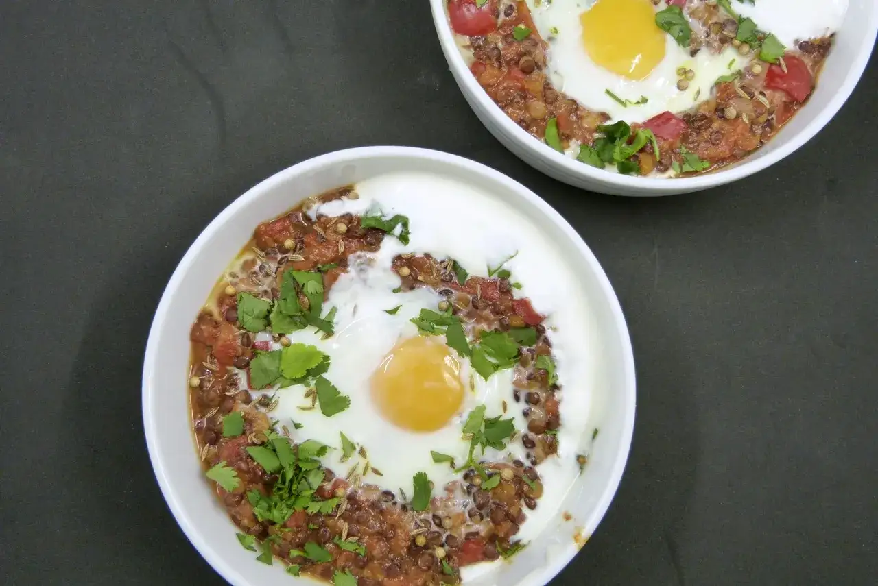 Zwei Schalen mit Linsen-Eintopf, garniert mit Koriander und einem Spiegelei. Ein leckeres Gericht, das zeigt, wie vielseitig Linsen Rezepte sein können.