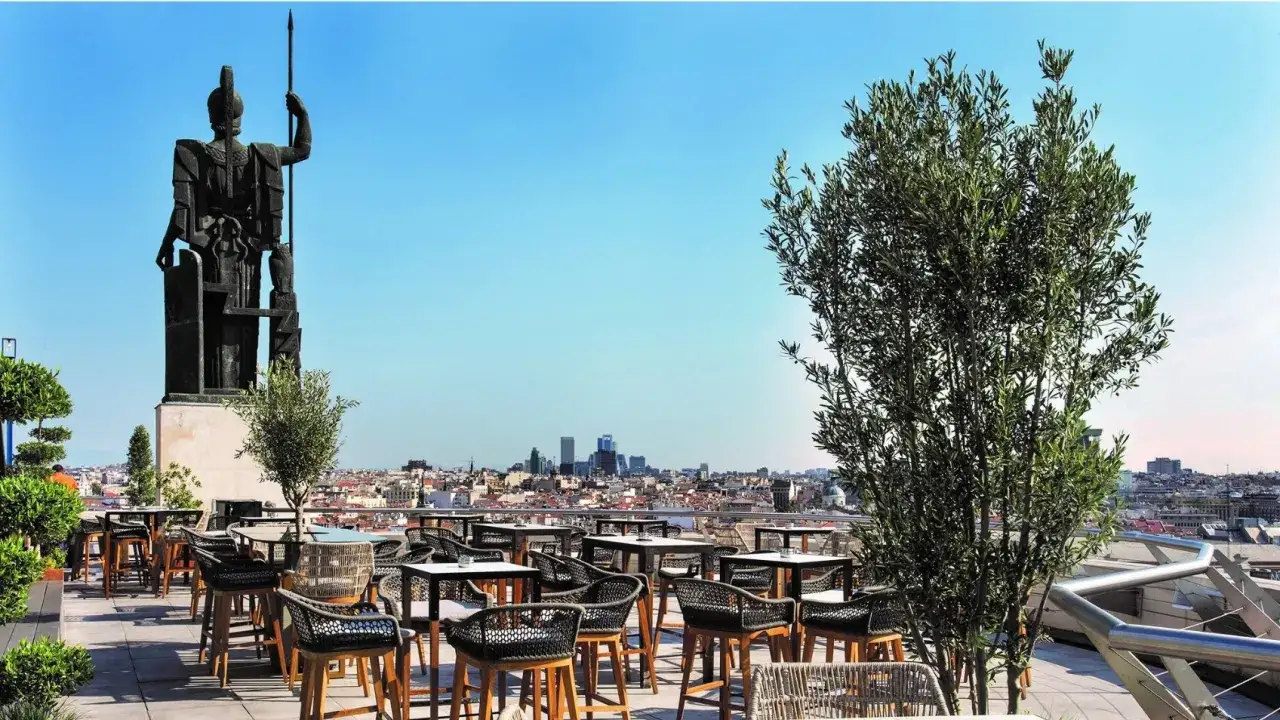 Terraza Bellas Artes Madrid con vistas a la ciudad. Una estatua monumental preside el espacio, rodeado de mesas y sillas de diseño.