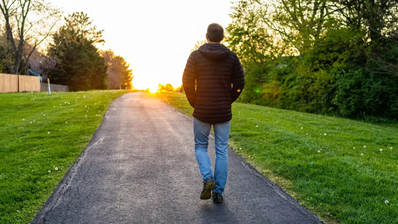 Hombre camina por un sendero al atardecer, disfrutando de un paseo tranquilo después de comer.