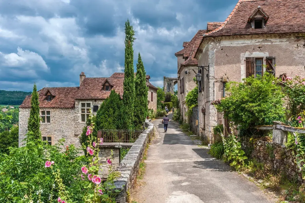 Un hombre camina por un pintoresco pueblo franc&eacute;s, rodeado de casas de piedra y vegetaci&oacute;n exuberante. Un ejemplo de la calidad de vida en Francia.